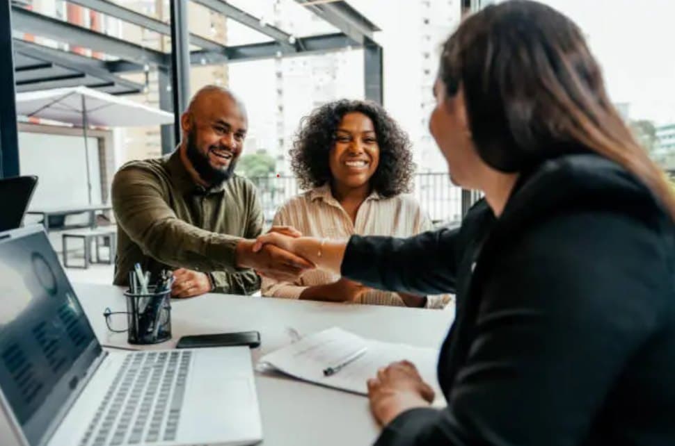 A broker shaking hands with clients across a desk.